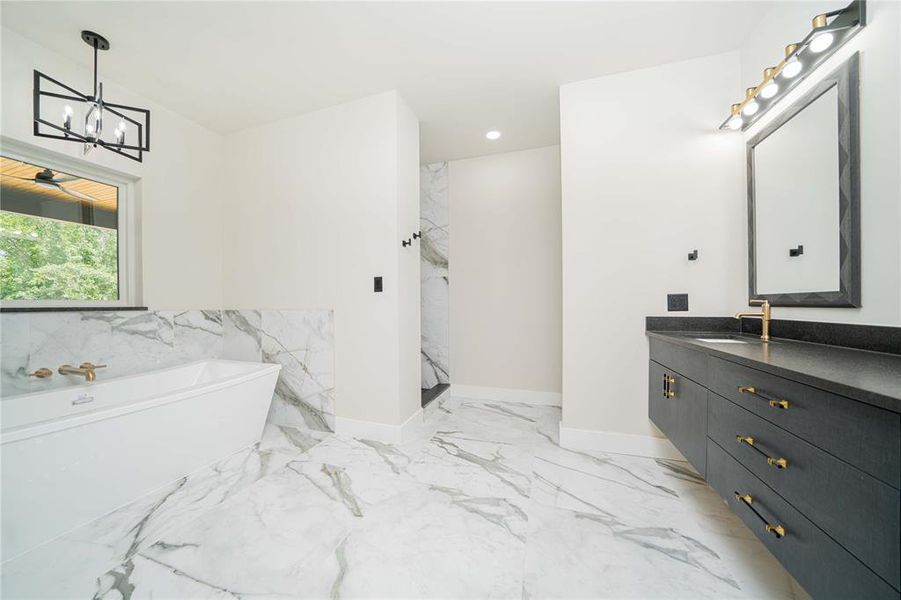 Full bathroom featuring marble look tile flooring, a soaking tub, vanity, a chandelier, and a marble finish shower Full bathroom featuring marble look tile flooring, a soaking tub, vanity, a chandelier, and a marble finish shower
