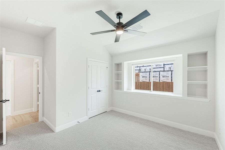 Empty bedroom with vaulted ceiling, ceiling fan, built-in shelves, and carpet flooring