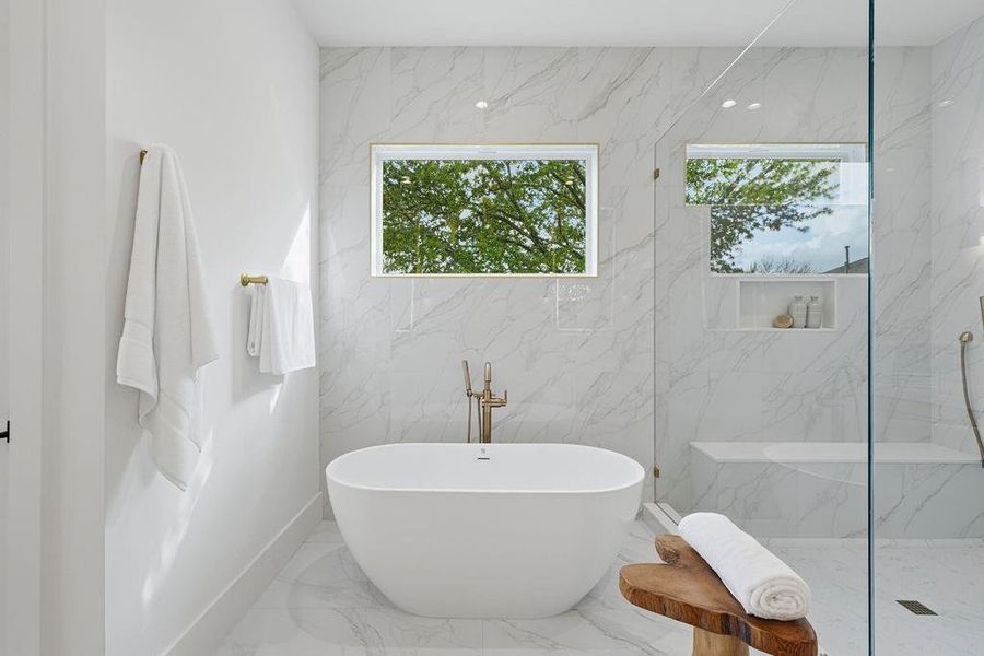Sculptural, egg-shaped freestanding soaking tub. Positioned against a flawless floor-to-ceiling slab of high-vein Carrara marble, the tub provides a moment of organic contrast to the bathroom's sleek architecture. This area is the epitome of thoughtful design, framed by a view of lush exterior greenery through the high-placed