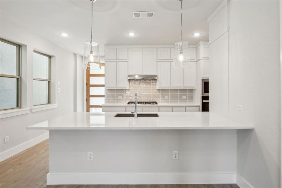 Kitchen featuring decorative light fixtures, white cabinetry, sink, decorative backsplash, and light hardwood / wood-style flooring