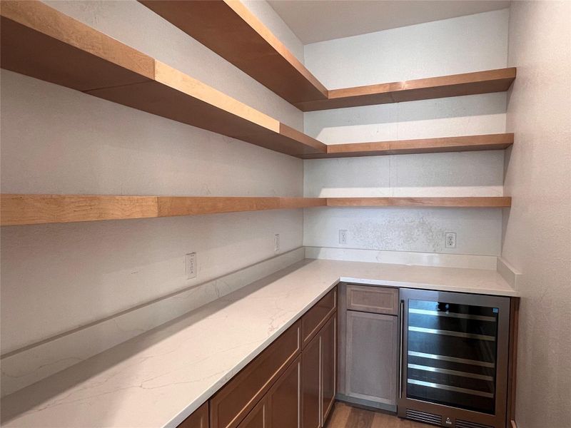 Bar featuring wine cooler, light stone countertops, open shelves, and light wood finished floors