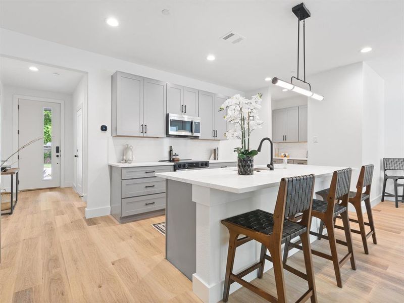Kitchen with a kitchen breakfast bar, light countertops, gray cabinets, stainless steel microwave, and range with electric cooktop