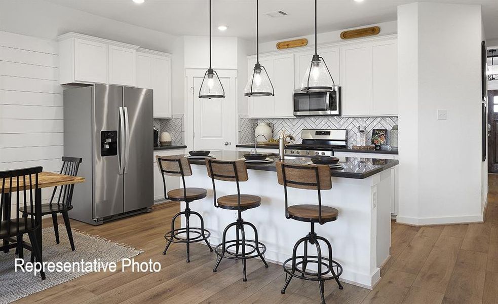 Kitchen featuring tasteful backsplash, a kitchen island with sink, light hardwood / wood-style floors, hanging light fixtures, and appliances with stainless steel finishes