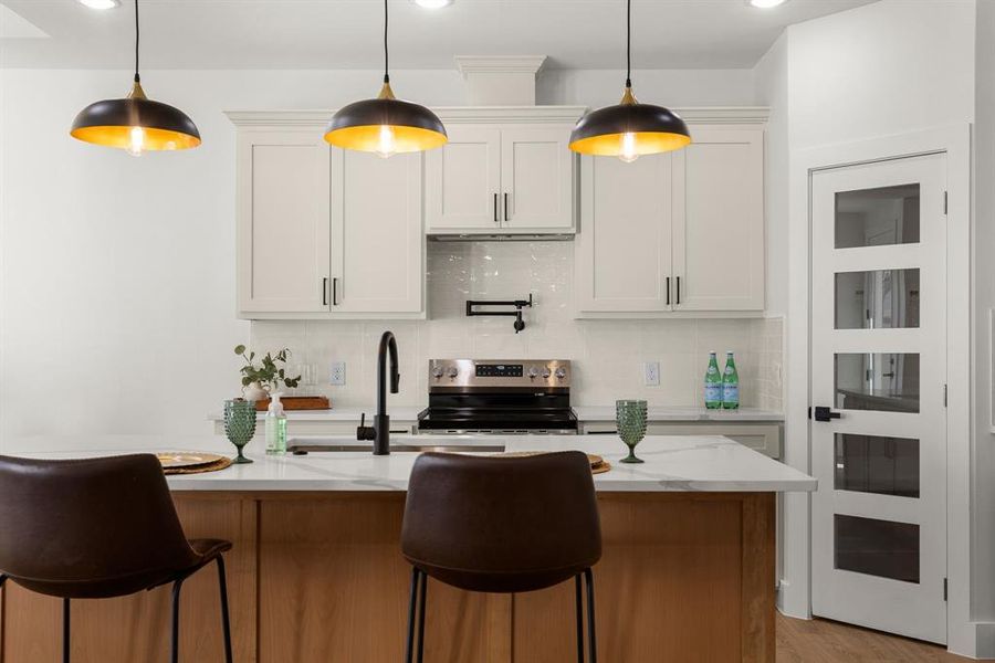 Kitchen with a sink, hanging light fixtures, backsplash, and stainless steel range with electric cooktop