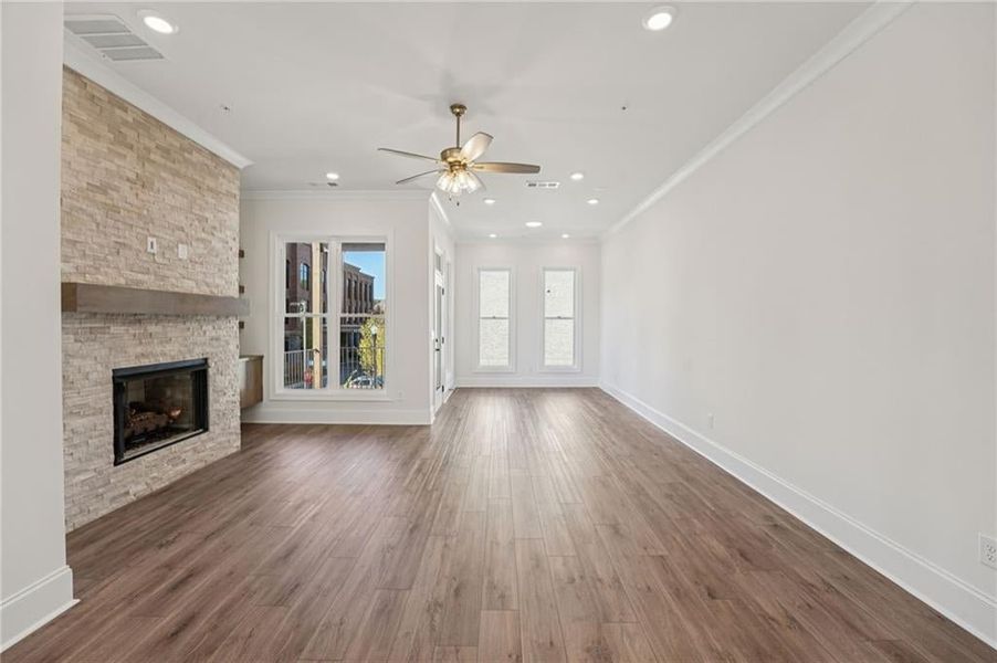 Living room, dining room an sunroom on Main level space features ornamental molding, a quartzite stone fireplace, wood flooring, ceiling fan, and plenty of light from large windows and added LED lights. This image is of a previously built Chamberlain Pla