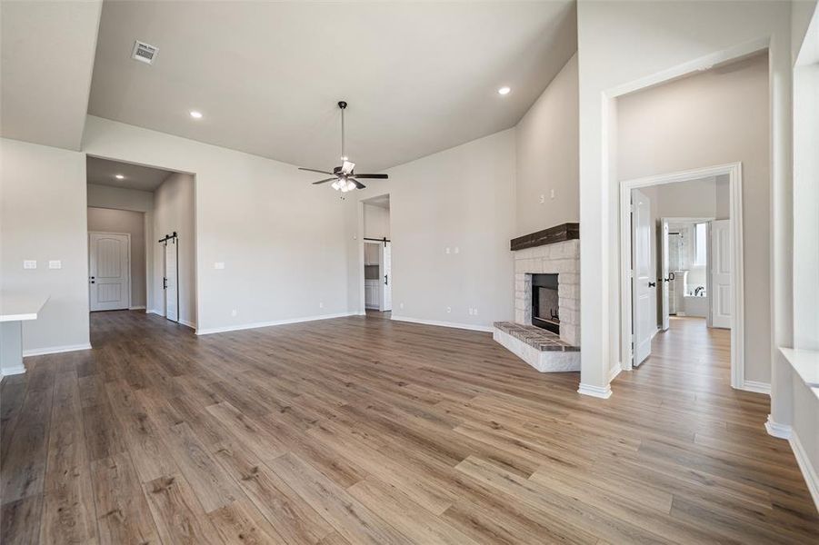 Unfurnished living room with a fireplace, light wood finished floors, recessed lighting, a ceiling fan, and a barn door