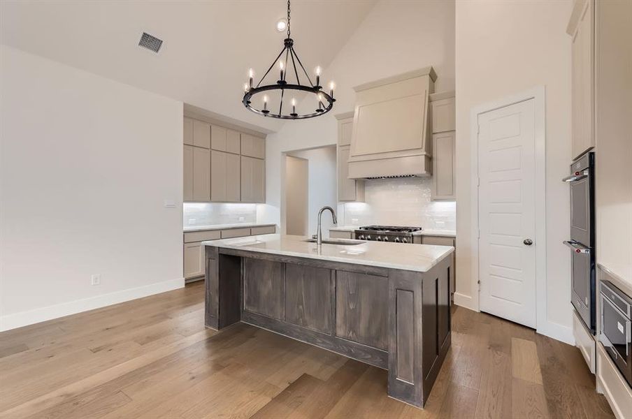 Kitchen featuring high vaulted ceiling, a chandelier, a center island with sink, and hardwood / wood-style floors