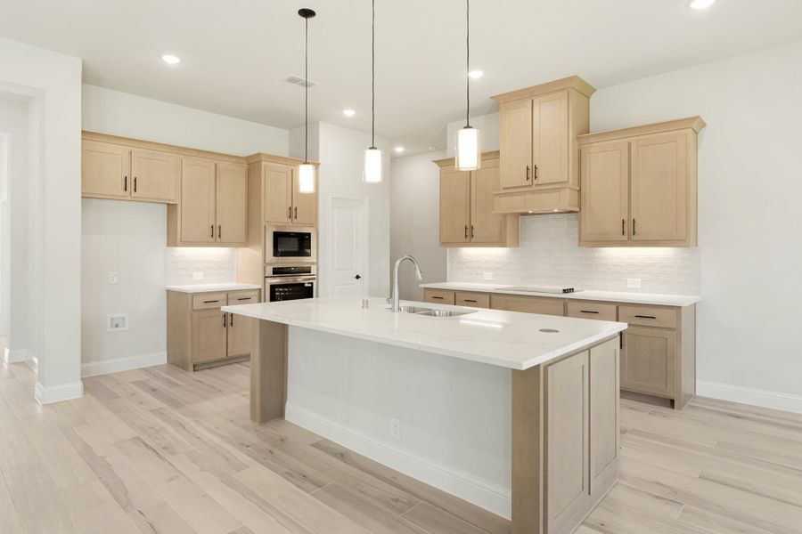 Open kitchen with light wood cabinets, large center island, white countertops, and pendant lights over light hardwood floors
