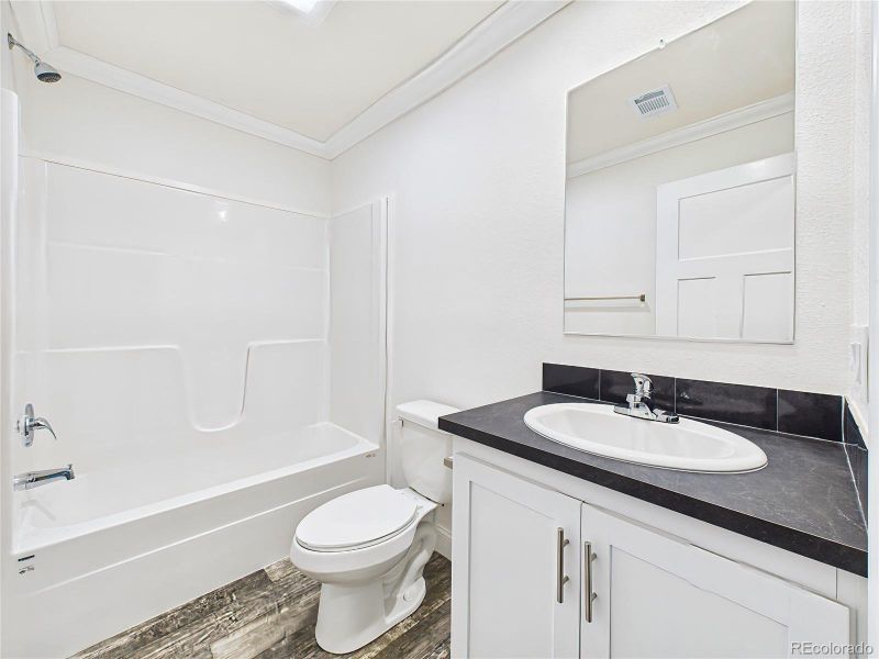 Full bath featuring white vanity with storage, modern black countertops, and a framed mirror. Tub/shower combo