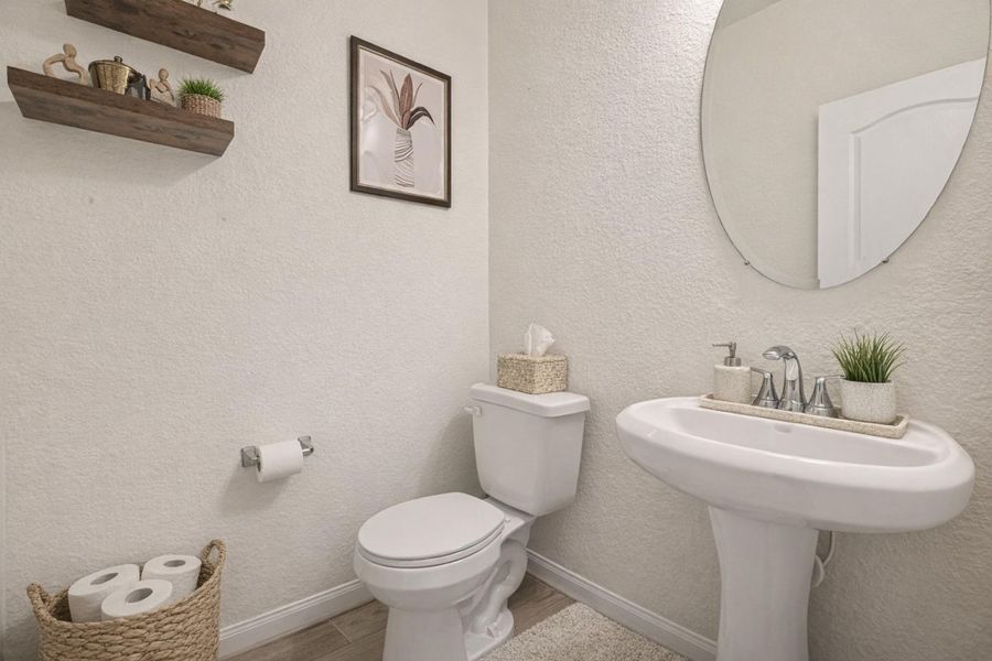 Stylish half bath featuring a pedestal sink, round mirror, and clean modern finishes.