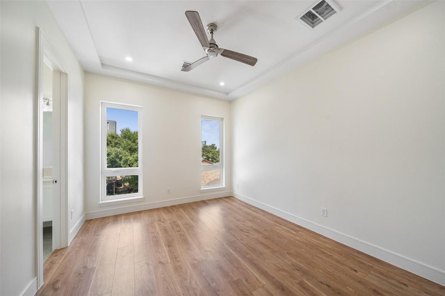 Secondary bedroom with wood floors, modern ceiling fan, recessed lighting, and two large windows offering plenty of natural light and views of greenery.
