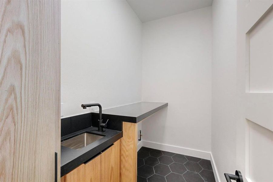 Utility space featuring a wood-finish cabinet, black countertop with integrated sink, matte black faucet, and hexagonal floor tiles Utility space featuring a wood-finish cabinet, black countertop with integrated sink, matte black faucet, and hexagonal floor tiles