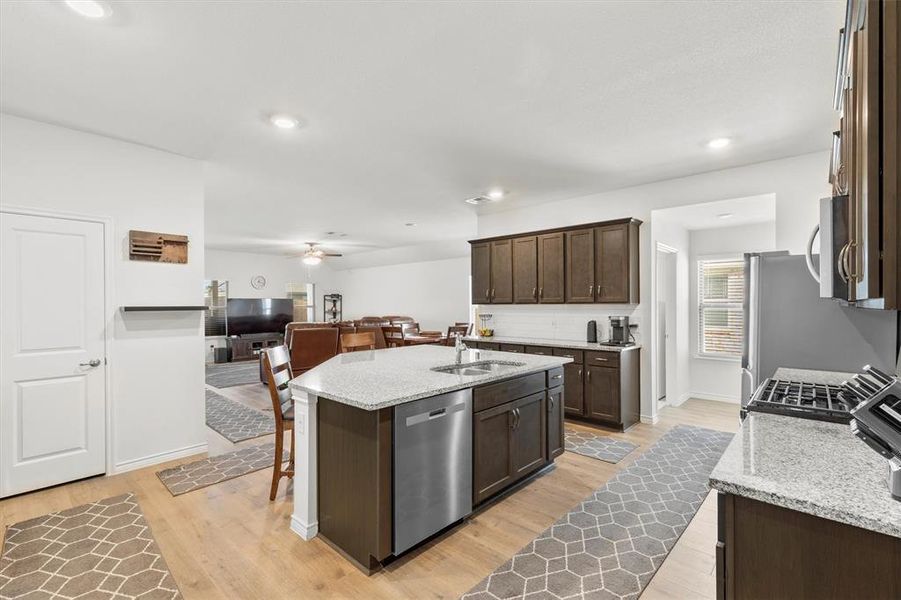 Kitchen featuring light stone counters, a kitchen breakfast bar, open floor plan, an island with sink, and light wood-style floors