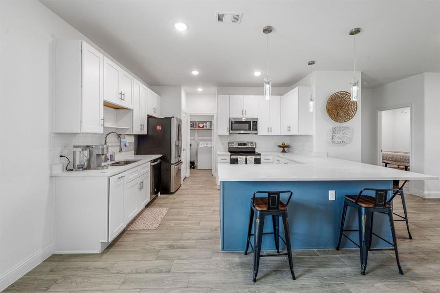 Kitchen with backsplash, a peninsula, appliances with stainless steel finishes, decorative light fixtures, and white cabinets