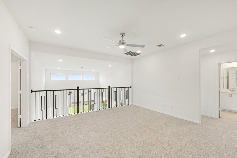 Open upstairs loft with carpet, ceiling fan, metal stair railing, and views to lower level and backyard.