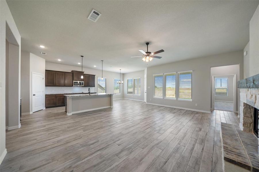 Unfurnished living room with a chandelier, a stone fireplace, light wood-style flooring, recessed lighting, and a ceiling fan Unfurnished living room with a chandelier, a stone fireplace, light wood-style flooring, recessed lighting, and a ceiling fan
