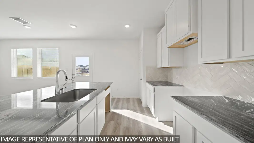 Kitchen featuring a large island with an undermount sink and gooseneck faucet, white shaker-style cabinetry, dark gray countertop surfaces, a light-toned herringbone tile backsplash, and light wood-finish flooring