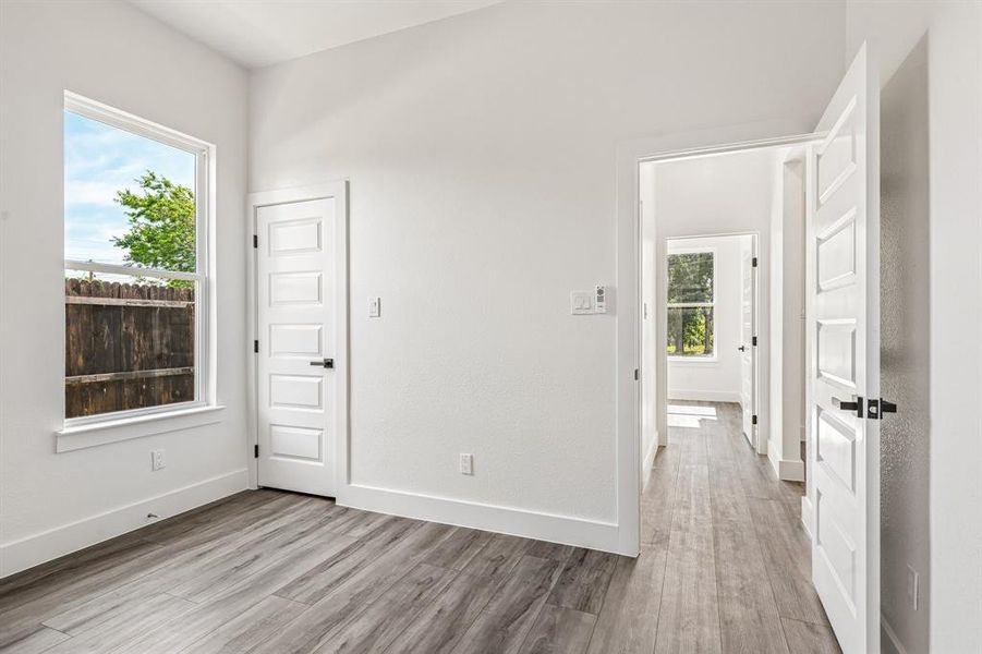 Spacious interior room featuring wood-finish flooring, white trim, and a five-panel interior door