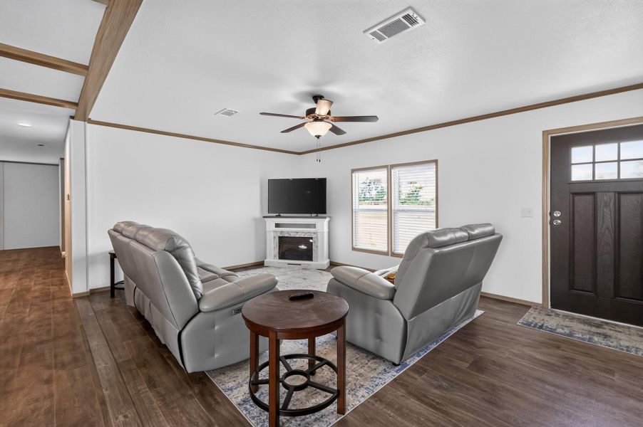 A welcoming living area features rich wood flooring, a ceiling fan, and a charming fireplace focal point.