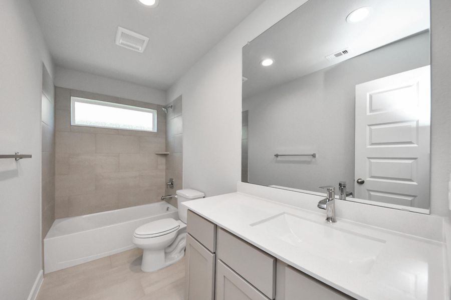 Secondary bath features tile flooring, bath/shower combo with tile surround, light stained wood cabinets, beautiful light countertop. Sample photo of completed home with similar floor plan. Actual colors and selections may vary.
