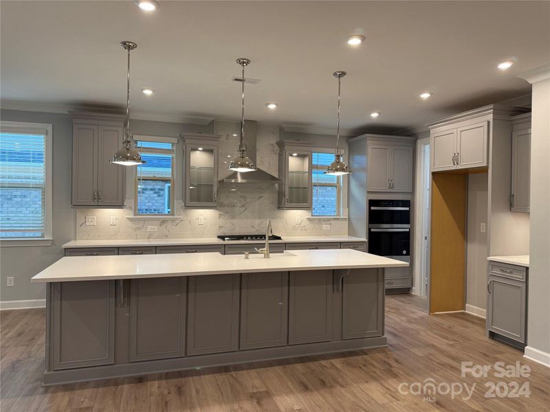 Kitchen features farmhouse sink, gas cooktop, under cabinet lighting, stainless steel range hood