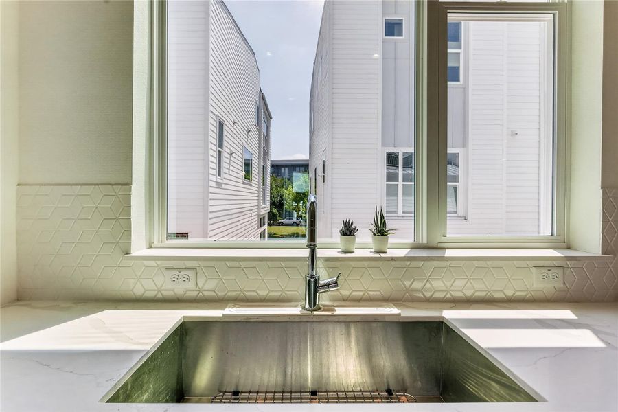 A deep basin sink with elegant backsplash tilework offers a practical and clean kitchen space.