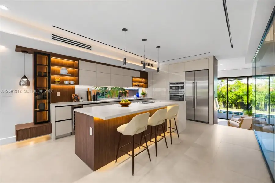 Modern kitchen featuring high-gloss cabinetry, stone-finish countertops, wood-finish island with integrated base lighting, stainless steel appliances, and minimalist pendant lighting Modern kitchen featuring high-gloss cabinetry, stone-finish countertops, wood-finish island with integrated base lighting, stainless steel appliances, and minimalist pendant lighting