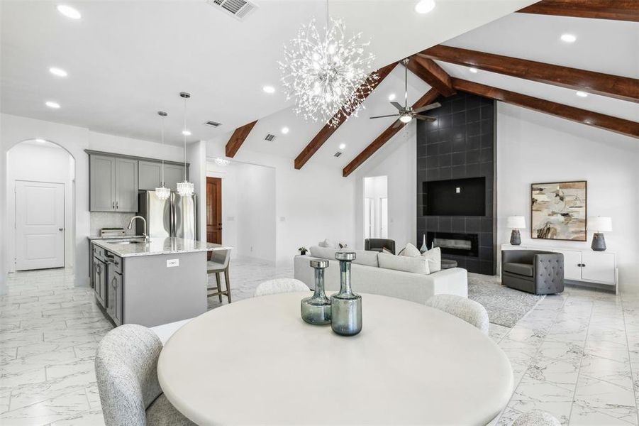 Dining room with beam ceiling, a tiled fireplace, ceiling fan with notable chandelier, and light tile patterned floors