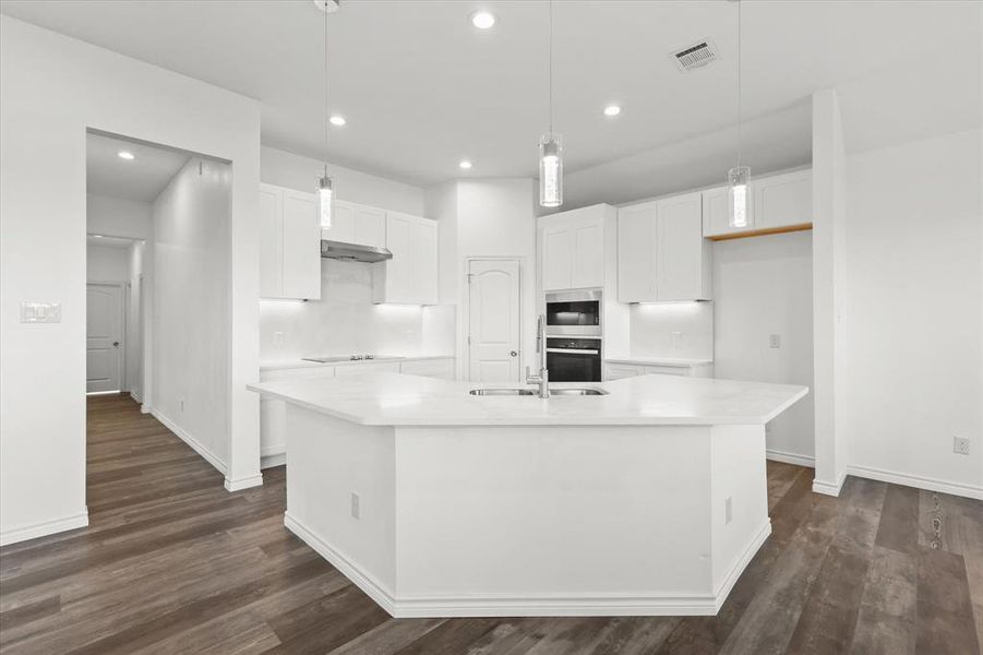 Kitchen with dark hardwood / wood-style flooring, white cabinets, and an island with sink