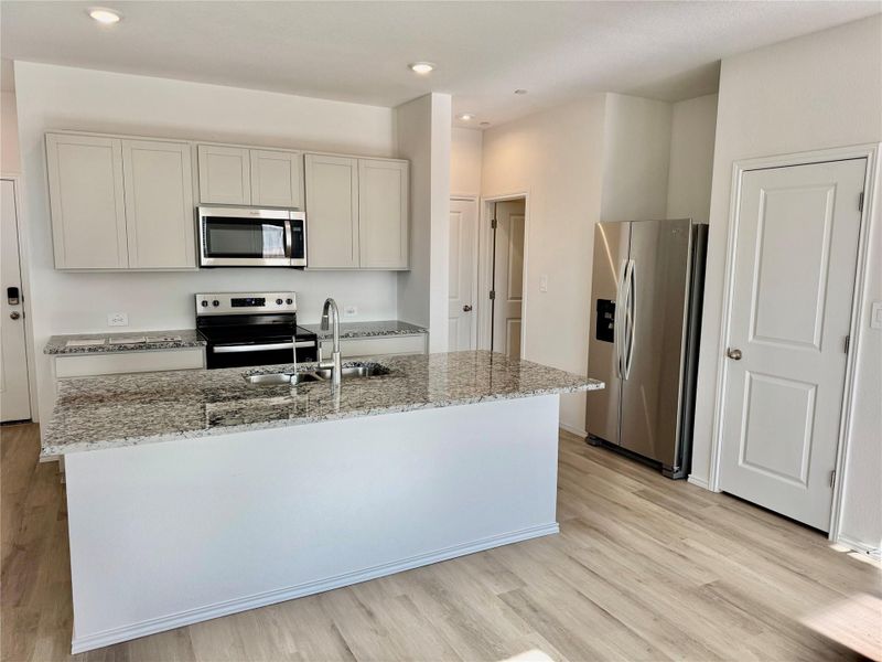 Kitchen with stainless steel appliances, light stone countertops, a kitchen island with sink, light wood-type flooring, and recessed lighting