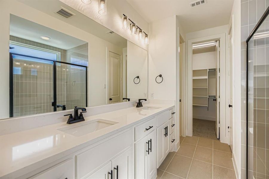 Full bathroom with a stall shower, double vanity, light tile patterned floors, and a spacious closet Full bathroom with a stall shower, double vanity, light tile patterned floors, and a spacious closet