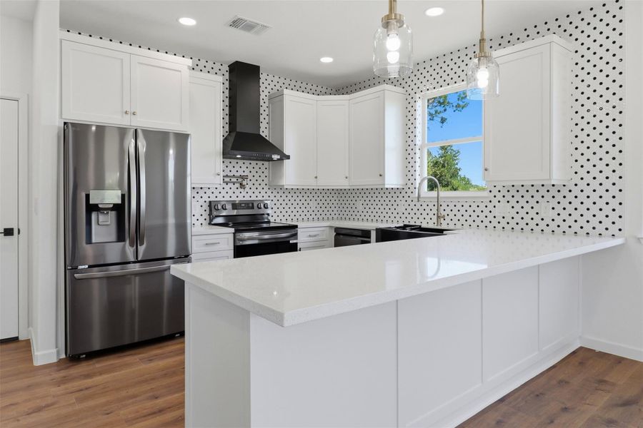 Modern kitchen featuring white cabinetry, a large white countertop island, stainless steel refrigerator, black range hood, and distinctive polka-dot tile backsplash Modern kitchen featuring white cabinetry, a large white countertop island, stainless steel refrigerator, black range hood, and distinctive polka-dot tile backsplash