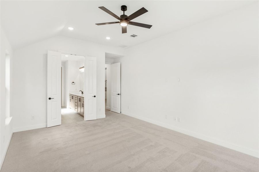 Empty bedroom with carpet, ceiling fan, and open doors leading to ensuite bathroom