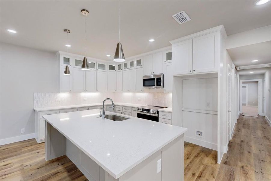 Kitchen featuring sink, stainless steel appliances, an island with sink, pendant lighting, and white cabinets