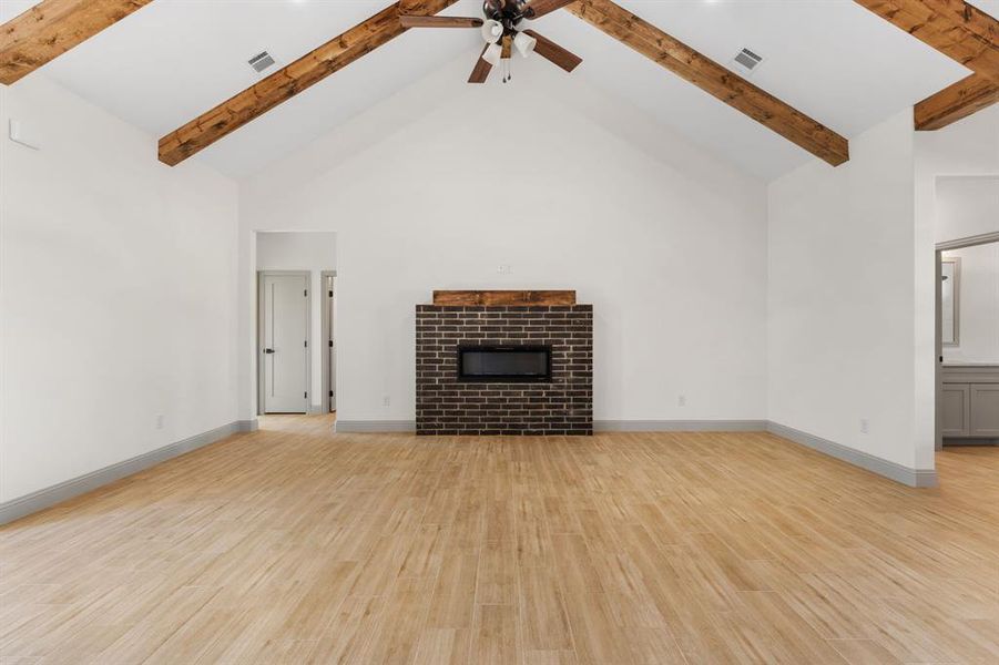 Unfurnished living room featuring high vaulted ceiling, a tiled fireplace, ceiling fan, light wood-style floors, and beam ceiling