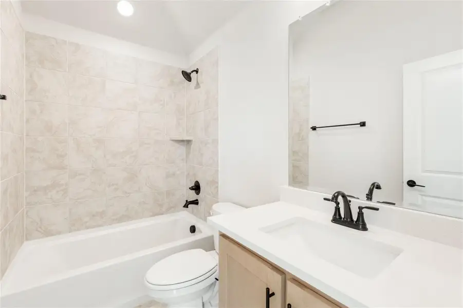 Full bathroom with tiled tub-shower combo, single vanity with white countertop, and black fixtures
