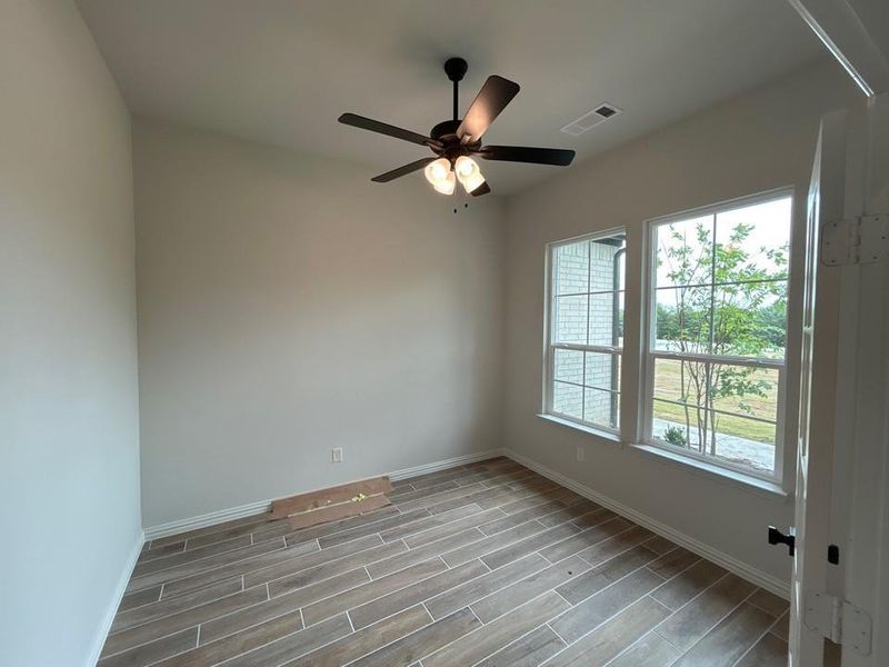 Room featuring wood-finish tile flooring, a dark bronze ceiling fan with integrated lighting, and two double-hung windows