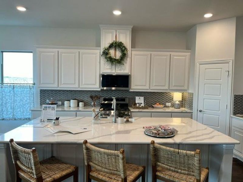 Kitchen featuring a kitchen bar, backsplash, white cabinetry, light stone counters, and recessed lighting Kitchen featuring a kitchen bar, backsplash, white cabinetry, light stone counters, and recessed lighting