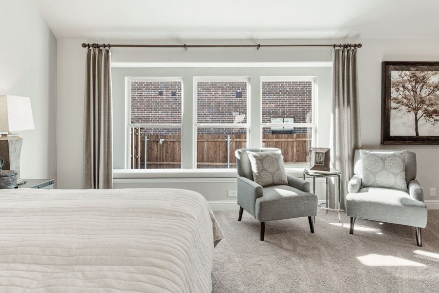 Bedroom with two gray accent chairs, large triple window with drapes, and carpeted floor