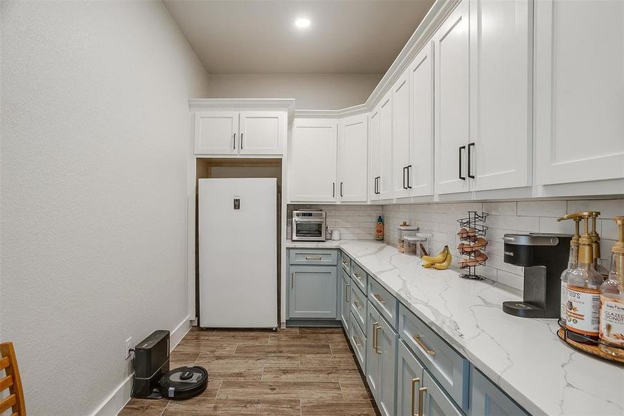 Kitchen featuring light stone counters, tasteful backsplash, light wood-type flooring, white refrigerator, and white cabinets