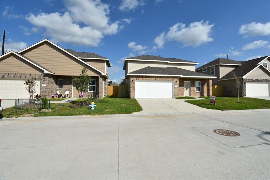 A suburban street with new single-family homes, clear skies, and a manicured lawn.