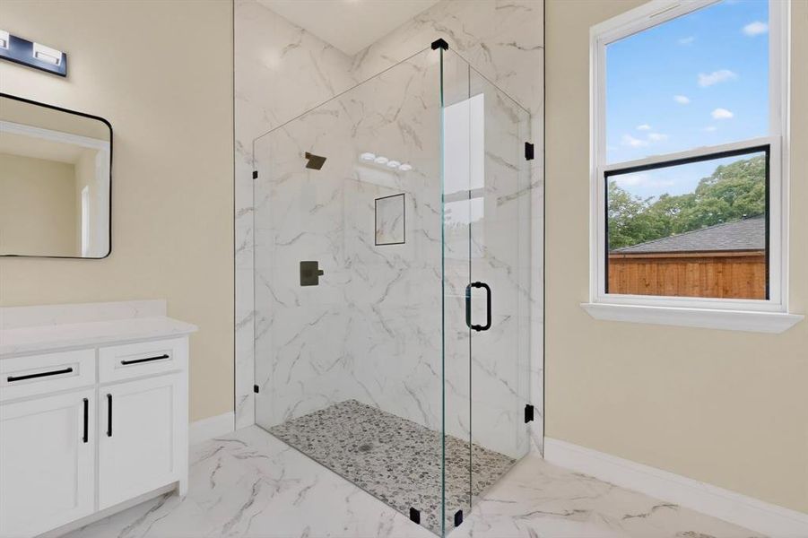 Glass-enclosed shower featuring large format tile surrounds and a pebble floor
