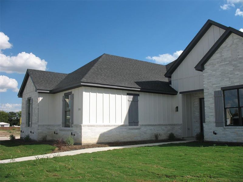 View of front of home featuring board and batten siding, a front yard, and roof with shingles