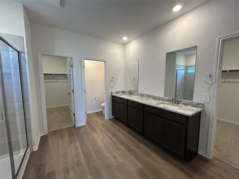 Full bath featuring a walk in closet, a shower stall, double vanity, dark wood-type flooring, and recessed lighting