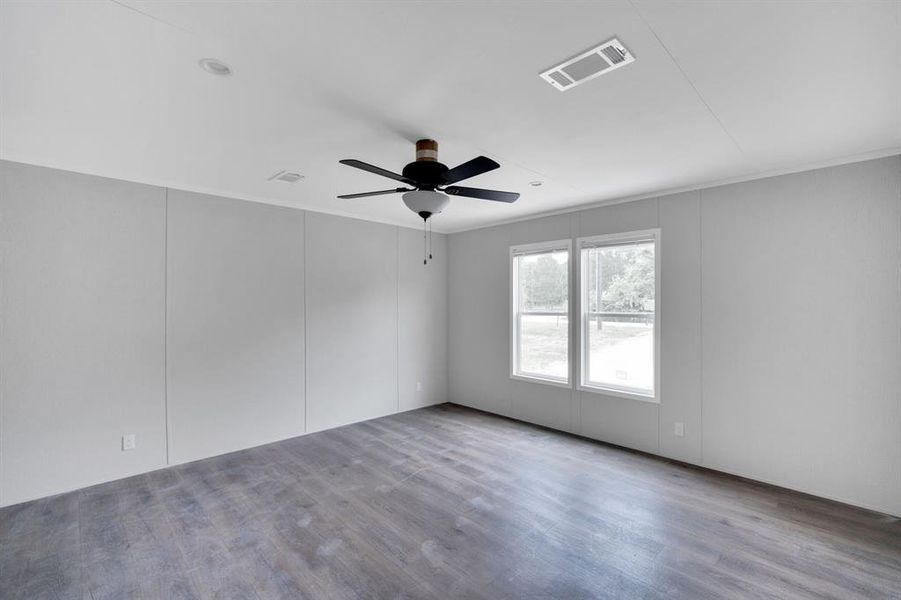 Spacious room featuring wood-finish flooring, light grey paneled walls, and a ceiling fan with integrated lighting