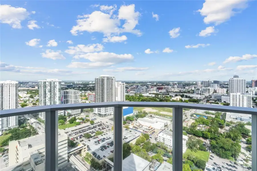 Private balcony featuring metal railings and a glass paneled enclosure overlooking an urban cityscape