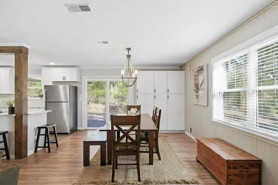 Dining area with wood-finish flooring, a contemporary chandelier, and a large window with blinds