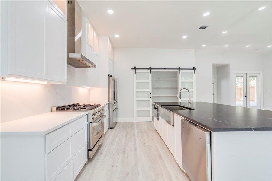 Kitchen featuring high quality appliances, range hood, a spacious island with sink, and recessed lighting