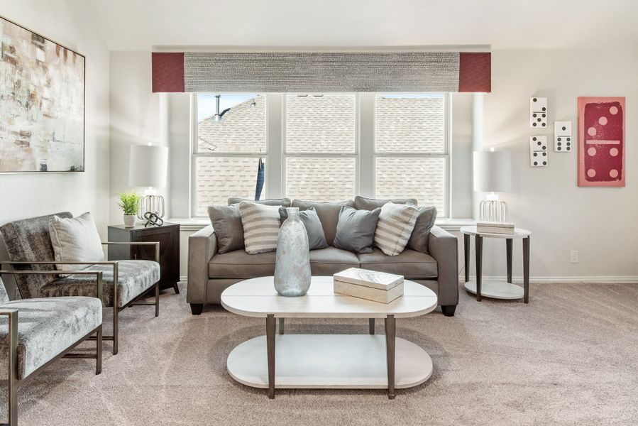 Living room with gray sofa, oval coffee table, and large window with roman shade over carpet flooring
