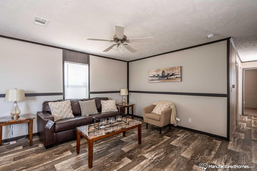 A comfortable living space featuring rich wood-look flooring and a functional ceiling fan.